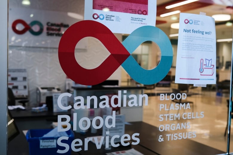 A glass door looking into a blood donation clinic features the Canadian Blood Services logo along with the name and the words blood, plasma, stem cells, organs and tissues.