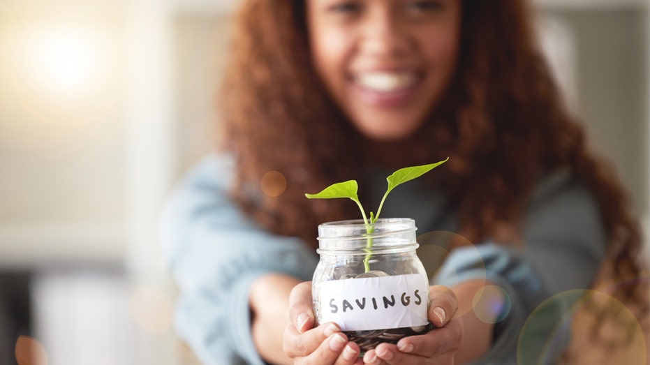 Woman holding a jar that says "savings" with a small plant growing out of the top