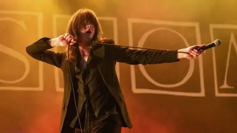 Getty Images Tom Ogden on stage with his hair over his eyes and one arm horizontally outstretched and holding the microphone away from him, at The Big Feastival 2023