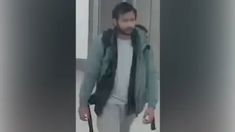 Northamptonshire Police CCTV of Pankaj Lamba wearing a green coat, white top and grey pants. He looks to have a backpack and is walking. 