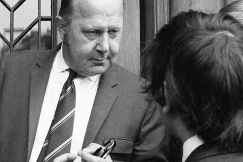 Getty Images Bank manager at the door of the bank, talking to a man. Both are wearing suits