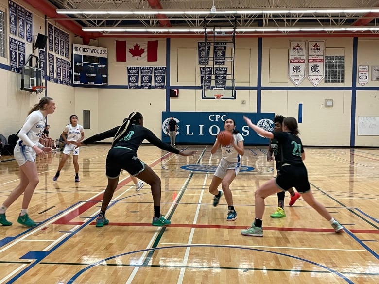 A high-school basketball player attempts a shot as two opponents defend.