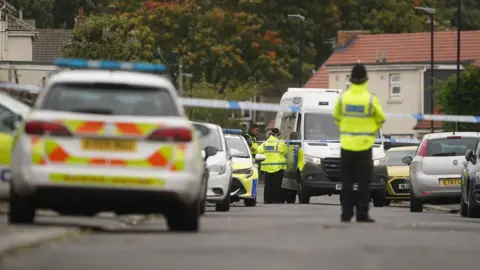 PA Media Police cars and police officers are dotted around a cordoned off residential street.