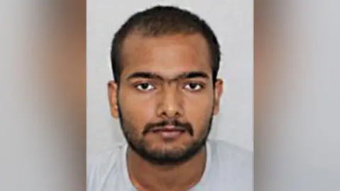 Northamptonshire Police Custody photo of Pankaj Lamba against a grey background. He has dark facial hair, brown eyes and is looking at the camera.