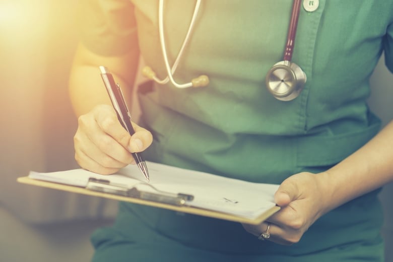 A stock photo of a nurse holding a clipboard and wearing scrubs.