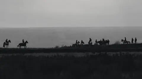 A black and white photo of a hunt, silhouetted against the sky