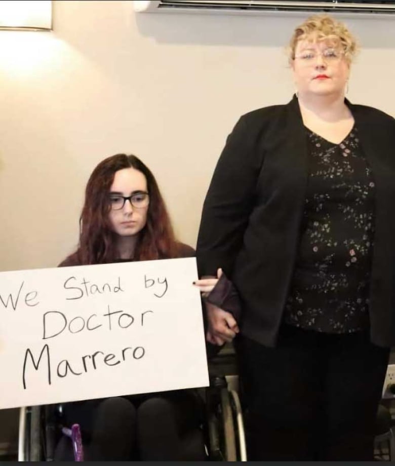 A young woman in a wheelchair holding a sign that reads, 'We stand by Doctor Marrero,' beside an older woman.