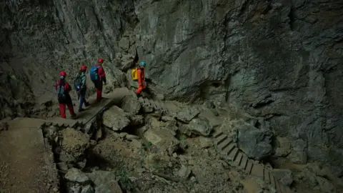 Xiqing Wang/ BBC  Four people climb down rock stairs into the hole