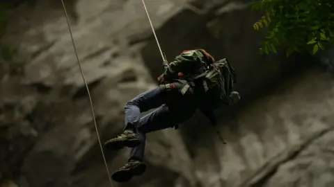 Xiqing Wang/BBC A person is lowered into a sinkhole