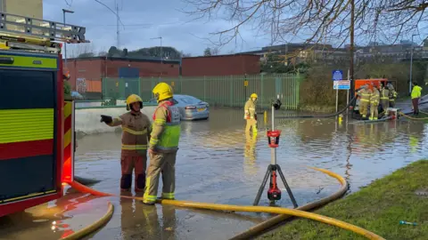 PA Media Firefighters in uniform work to pump water away from flooded residential streets near Moat Park in Dundonald on the outskirts of Belfast