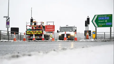 Reuters Roads vans and traffic bollards blocking an icy road with a red and white road closed sign visible