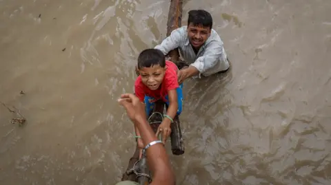 Reuters A man helps his son to climb on a flyover under construction after being displaced by the rising water level of river Yamuna after heavy monsoon rains in New Delhi, India. The man is in muddy water up to his waist.