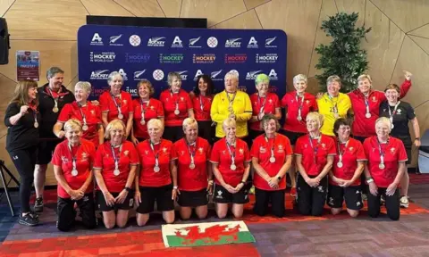 Jean Satterley Picture of the over 65s Hockey team, wearing medals around their necks and all in their red welsh jersey tops. 