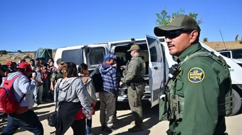 Getty Images Customs and Border Patrol agents load migrants into a vehicle after groups of migrants walked into the US from Mexico at Jacumba Hot Springs, California, on 5 June 2024. 