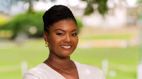 Tremaine Yearwood Brittney McKenzie, wearing gold hoop earrings,  a gold necklace and a white cardigan, poses for a photo