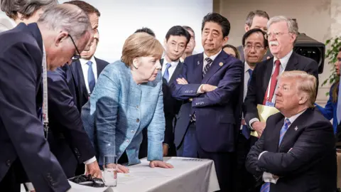 Getty Images Angela Merkel stares down a seated Donald Trump as a crowd of world leaders looks on, in an iconic image from the G7 Summit in Canada in 2018