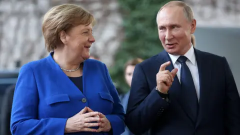 Getty Images Angela Merkel and Vladimir Putin smile as he speaks at a UN conference in 2020