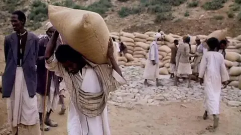 Scene of a man holding a sack of grain on his shoulders, from Michael Buerk's reporting in Ethiopia in 1984