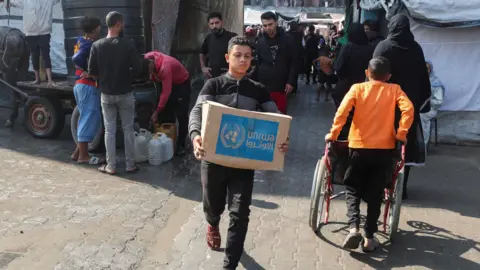 Reuters A Palestinian carries an aid box distributed by UNRWA in Deir al-Balah, central Gaza (4 November 2024)