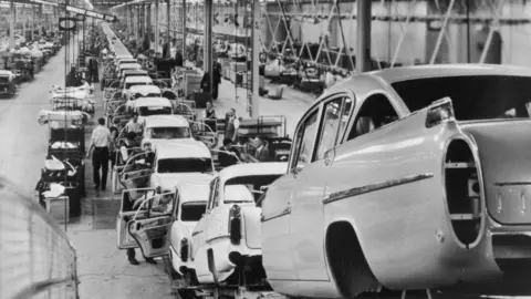 Getty Images The entrance to the assembly plant of the automotive manufacturing company IBC Vehicles Ltd, operating under Vauxhall Luton and producing light commercial vehicles, in December 2021. It shows blue metal gates, red barriers, and a grey building with lots of windows 