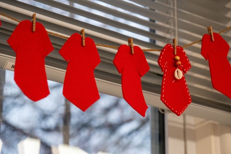 Five small red dresses made of felt are hung on a window.