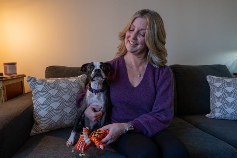 A person sits on a couch with a dog.