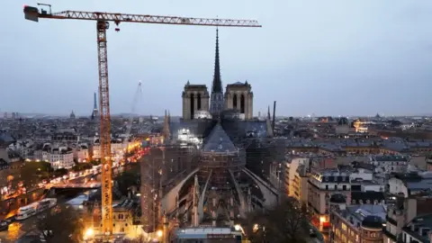 Getty Images This aerial photograph shows a crane next to scaffolding on Notre-Dame de Paris cathedral as the sun rises a few days before its reopening, on November 25, 2024. 