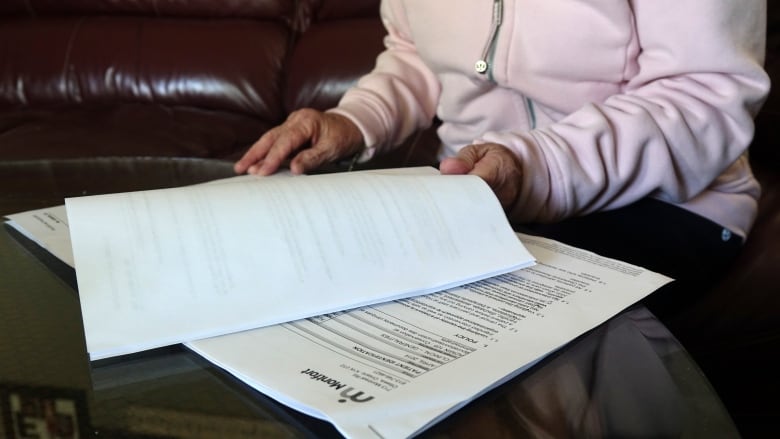 A close-up shot showing a woman in a pink hoodie sorting through pages stapled together.