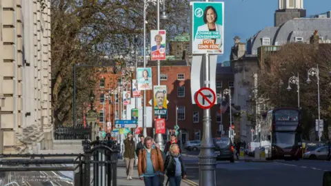 Getty Images Pedestrians walk along a street in Dublin which is covered in election posters along the lampposts