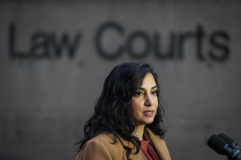 A South Asian woman with dark brown hair and a brown coat stands outside the courthouse.