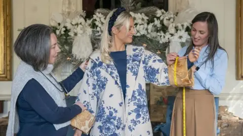 PA Media A woman wearing a kimono with two women measuring her arms