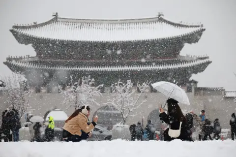 Kim Hong-Ji/Reuters A woman takes a photographs of her friend during heavy snow fall in central Seoul 
