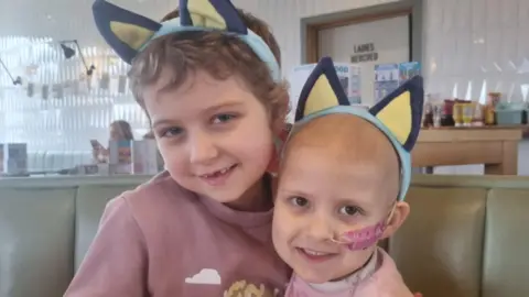 Family photo Betsy (left) and Lacie. Both are wearing headbands with animal ears. Lacie has lost her hair and has a tube up her nose. 