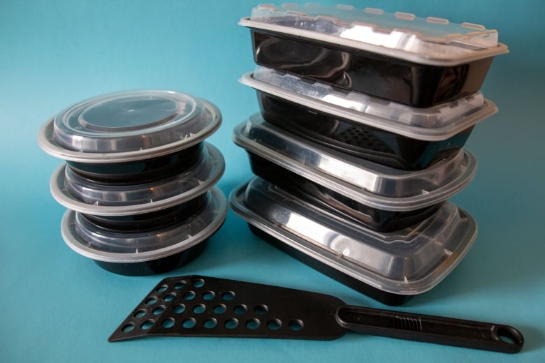 A stack of black plastic takeout containers and a single black plastic spatula.