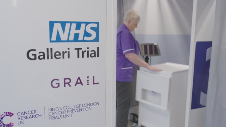 A still image from a video shows a sign saying 'NHS Galleri Trial - Grail - Cancer Research UK' outside a clinic room.