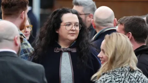 PA Media Storrie wearing glasses and a black cape with long curly hair in teh middle of a crowd