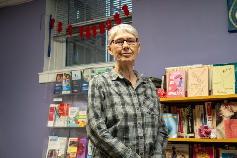 A person stands in a room in front of a bookshelf.