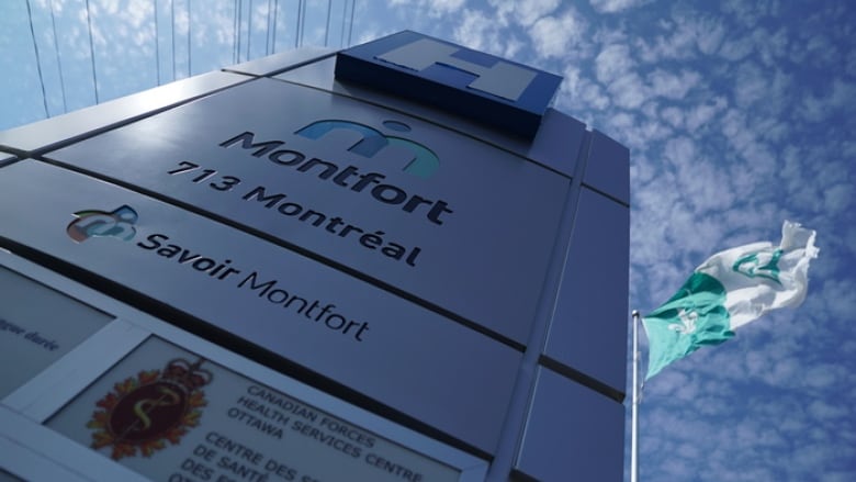 A sign for a hospital, with the Franco Ontarian flag flying behind it on a sunny day.