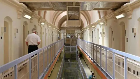 Getty Images A shot of a prison officer walking along inside a prison