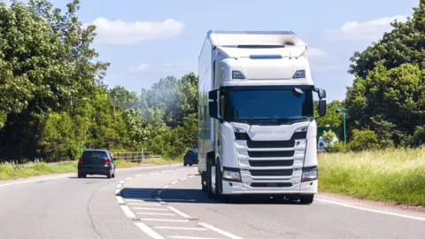 Getty Images A white lorry passes two black cars going along a single carriageway road lined by trees