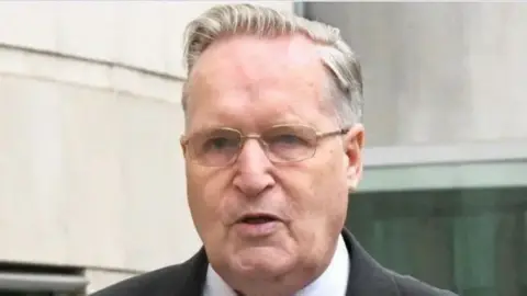 Photopress Close-up of Paul Dunleavy outside court. He has grey-ish hair, wearing glasses, black blazer and white shirt.