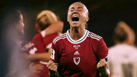 Getty Images Wales player Natasha Harding, now known as Allen-Wyatt, is wearing a Wales football shirt and celebrating a goal, pumping her fists. She is outlined in front of a graphic of a football pitch outline on top of a blurred still photograph of her playing football for Wales.