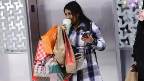 Getty Images A woman sips coffee in a store while holding multiple shopping bags on one arm