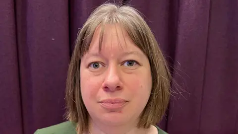 BBC Hilary Parker, a woman with short brown hair wearing a green top and standing in front of a purple curtain