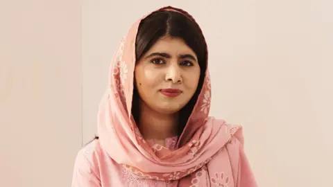 Getty Images Malala Yousafzai, posing for the camera while wearing traditional clothing in a pale pink colour with matching headscarf.  