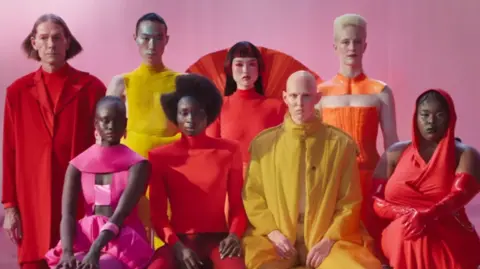 Jaguar Models in bright coloured clothes sit facing the camera and posing for an advert for Jaguar cars