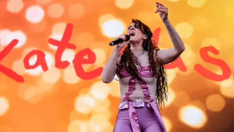 Getty Images Kate Nash singing on stage in a purple outfit against an orange backdrop with her name on it in giant letters