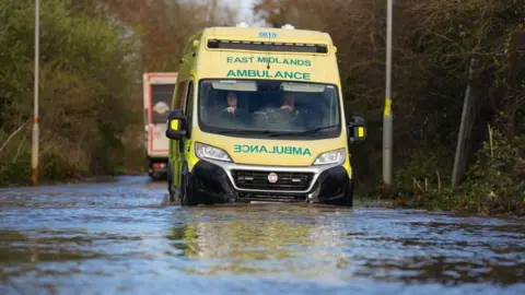 PA Media An ambulance drives through floodwater in Northamptonshire