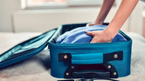 Getty Images A stock image of a person placing a blue jumper into a blue suitcase.