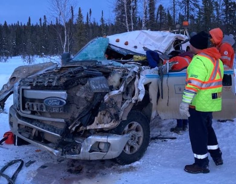 A mangled truck with people standing around it.